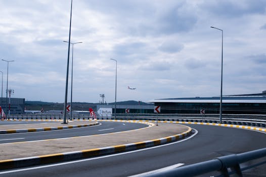 Airplane approaching the runway at modern airport, surrounded by curved roads and cloudy sky.