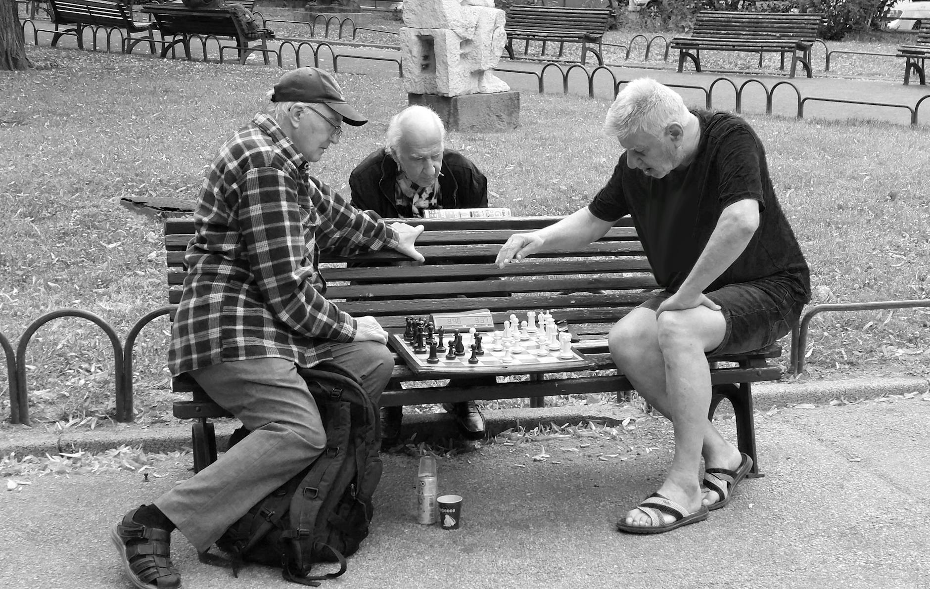 Three elderly men engaged in a serious chess game in a public park setting.