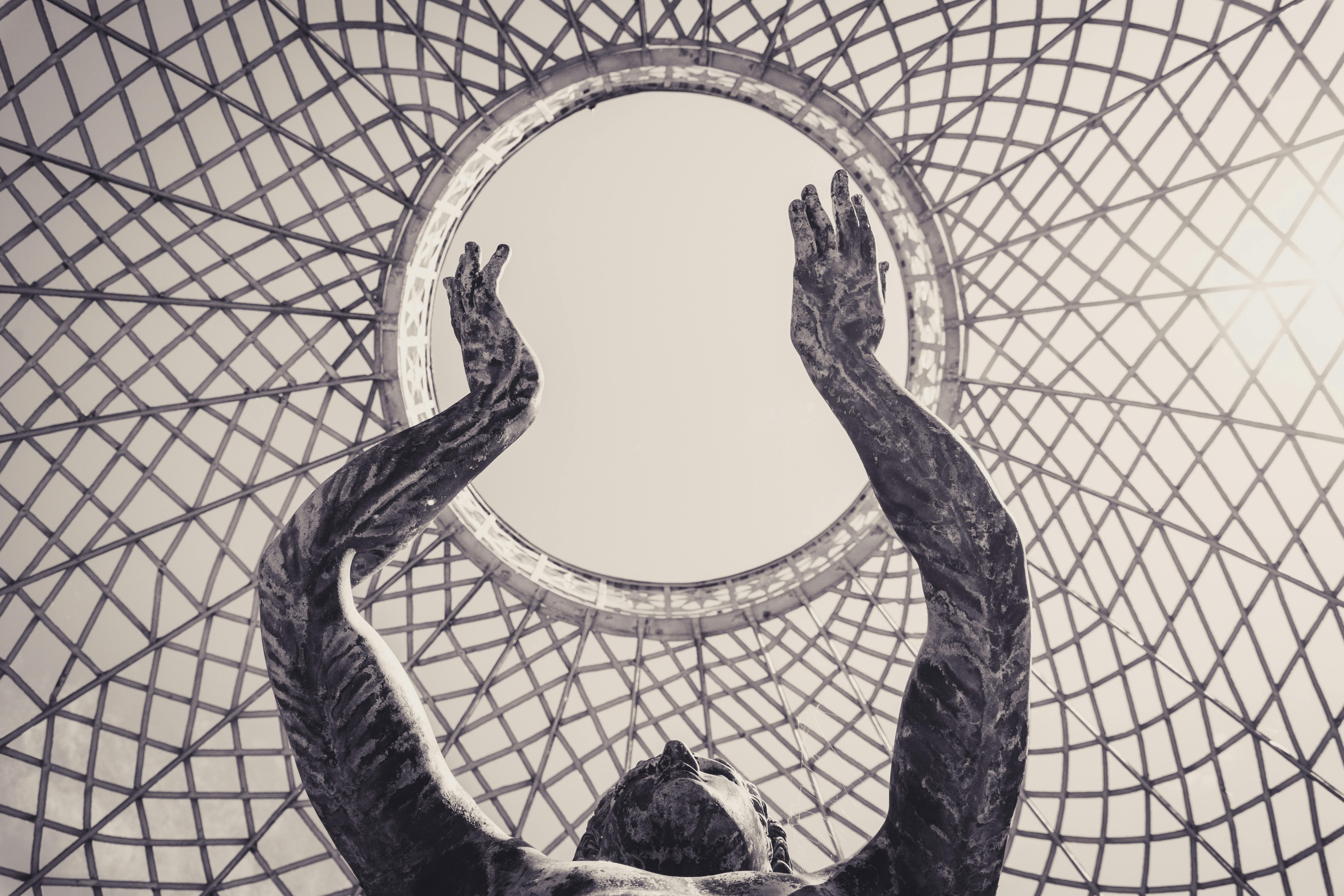 Free Dramatic sculpture reaching towards a circular sky framed by intricate lattice structure. Stock Photo