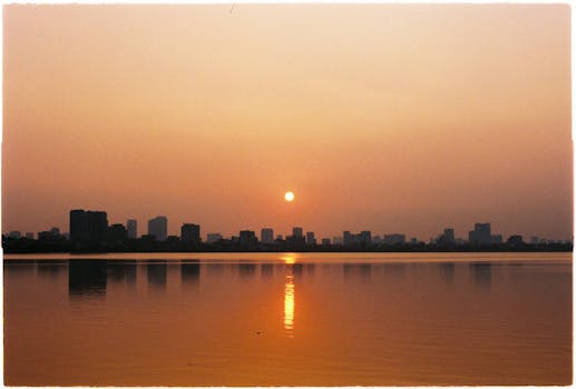 Serene sunset over Hanoi's West Lake, with city skyline reflections and warm hues lighting the sky.