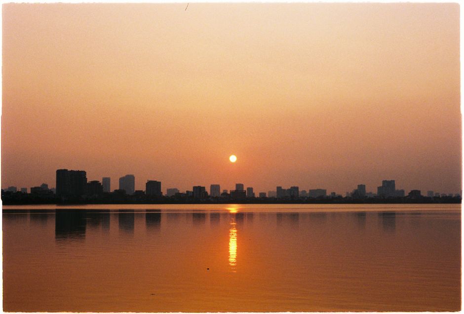 Serene sunset over Hanoi's West Lake, with city skyline reflections and warm hues lighting the sky.