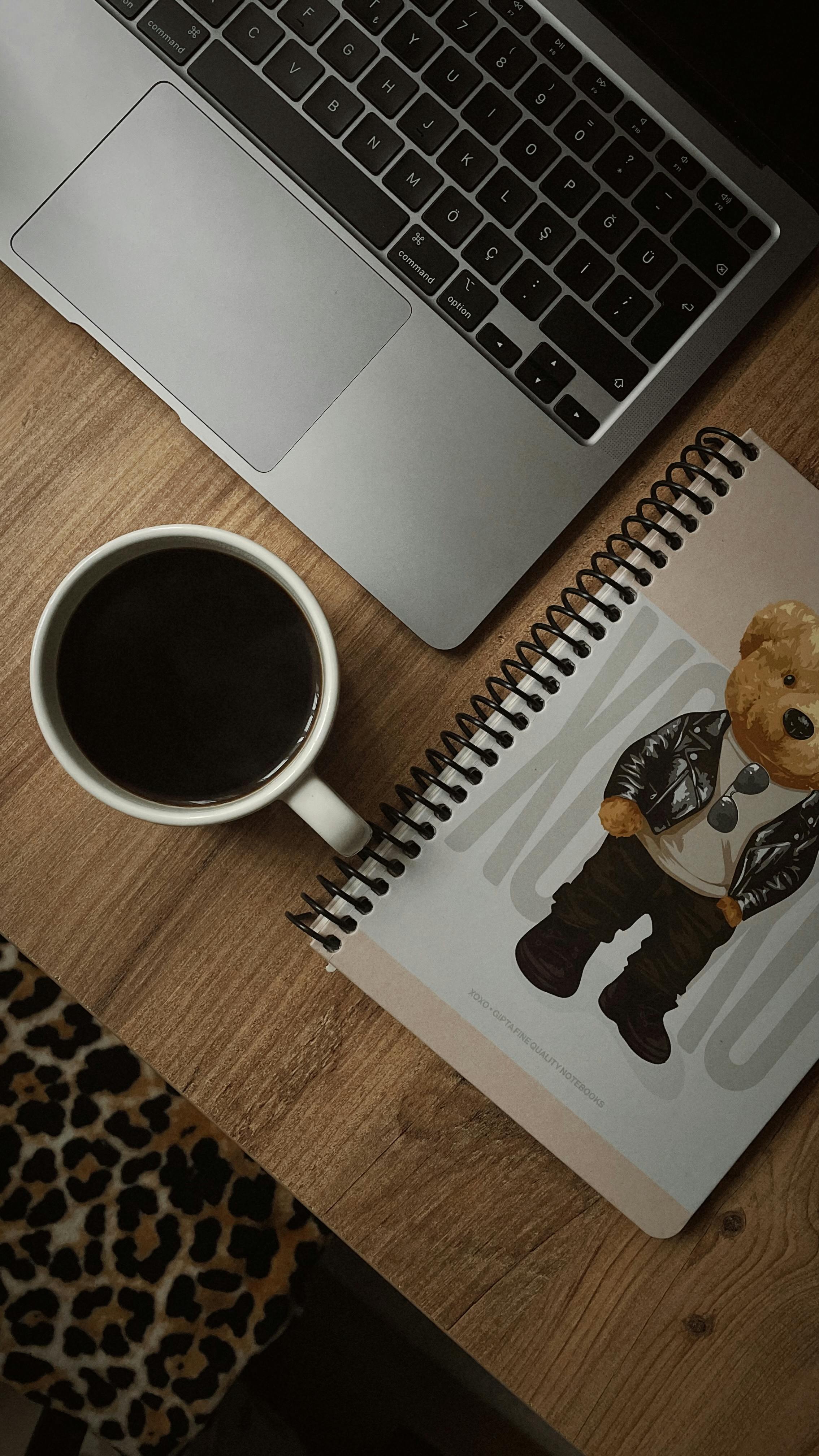 Cozy workspace featuring a laptop, coffee cup, and illustrated notebook on a wooden table.