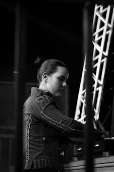 Black and white photo of a female DJ mixing at a live concert, with dramatic lighting.