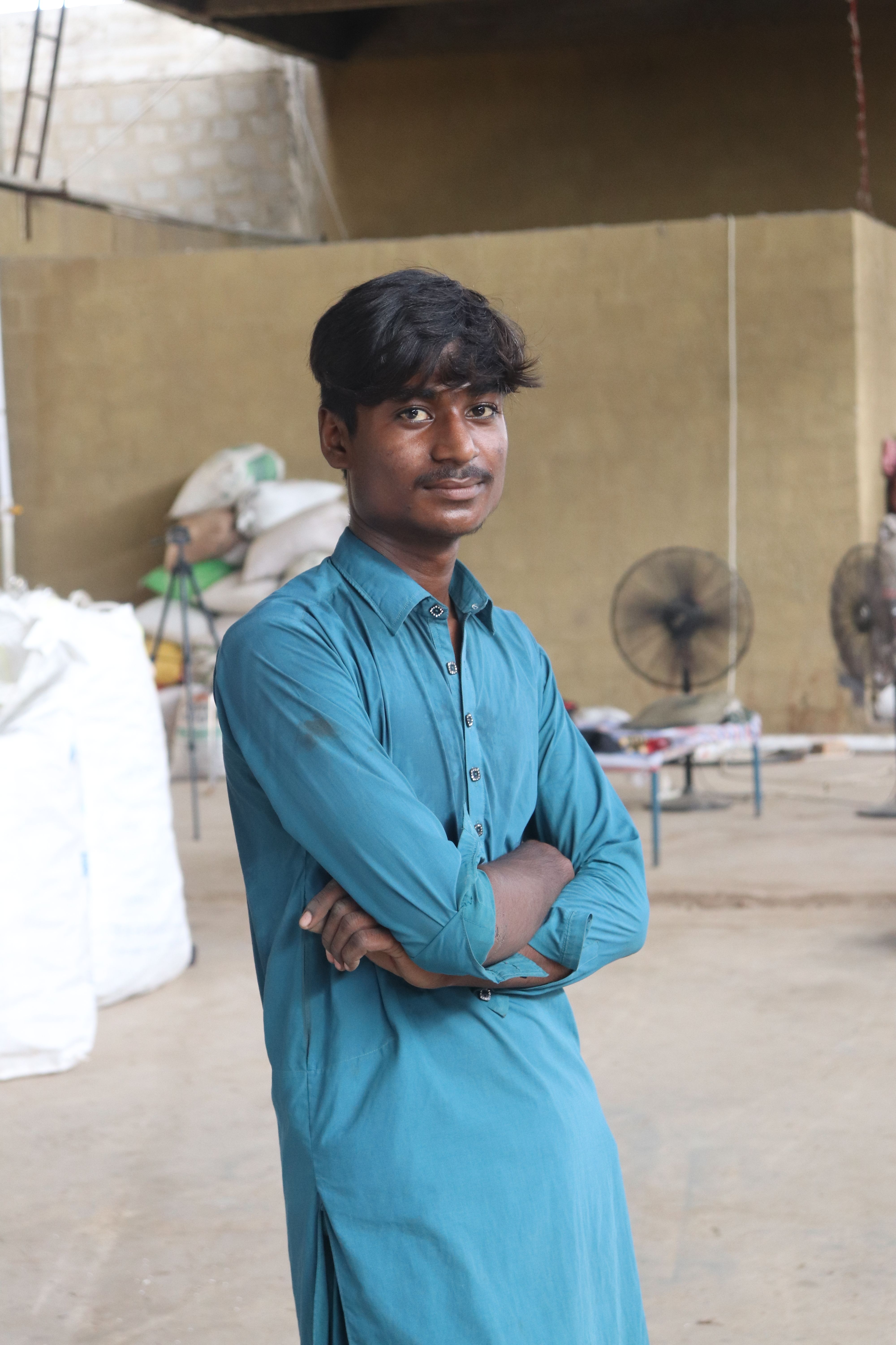 Portrait of a young man in a blue shirt posing confidently in an industrial area of Karachi, Pakistan.