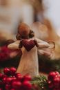 Decorative wooden angel holding red loving heart among red Christmas berries against blurred background