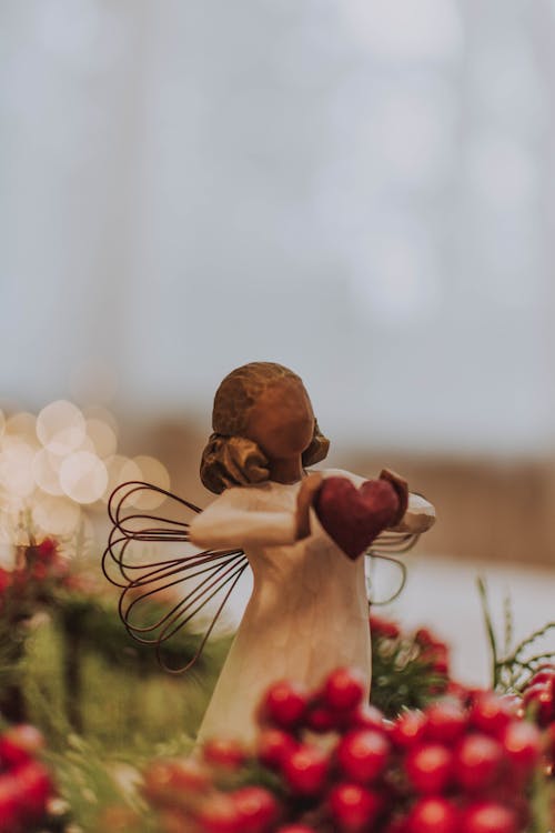 Wooden angel holding red heart among evergreens and berries