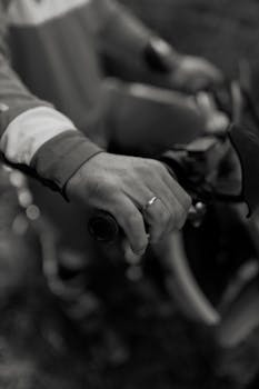 Artistic black and white image of a person gripping a bicycle handlebar. Captures motion and texture.