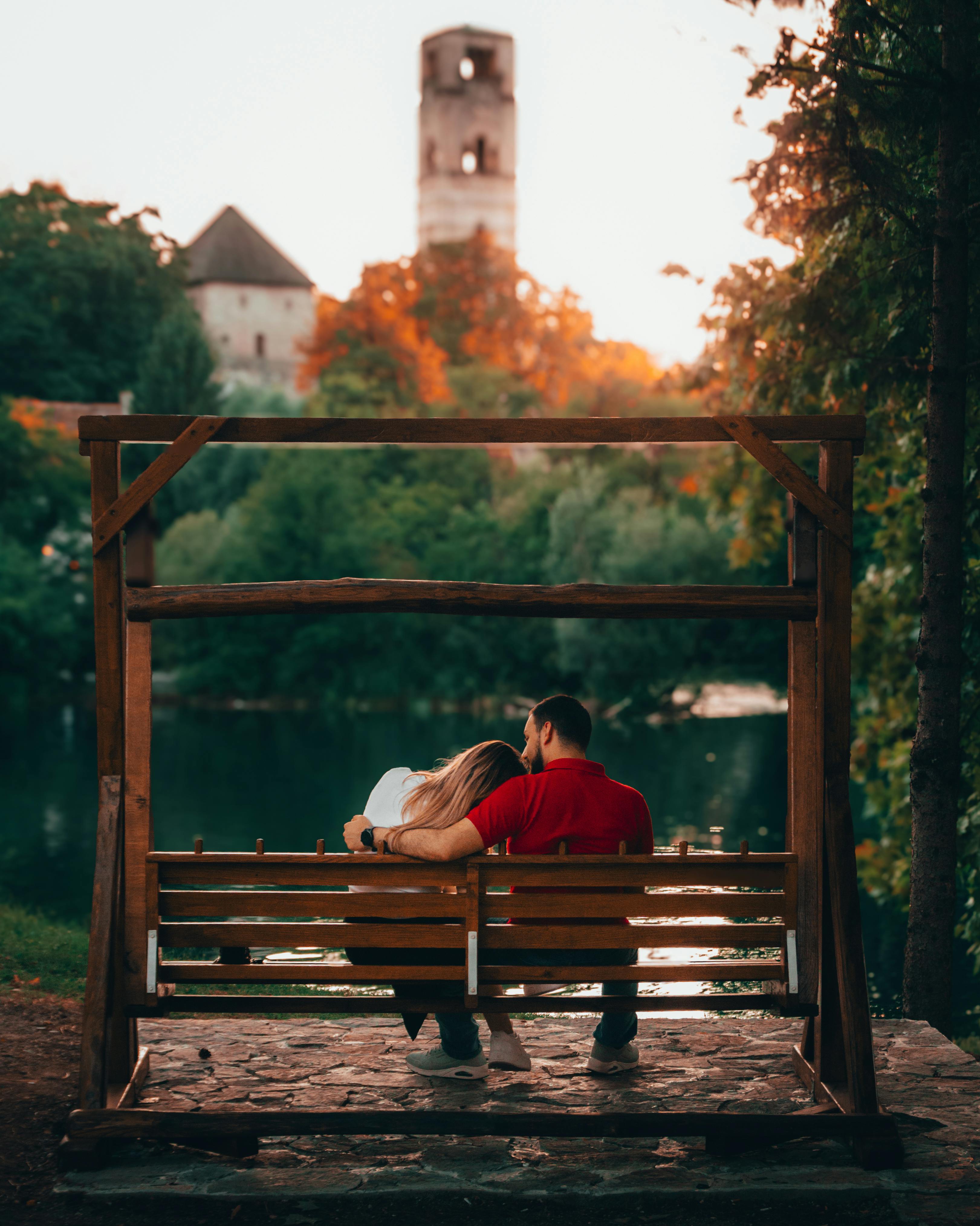 A couple enjoys a serene moment on a park bench with a castle view at sunset.