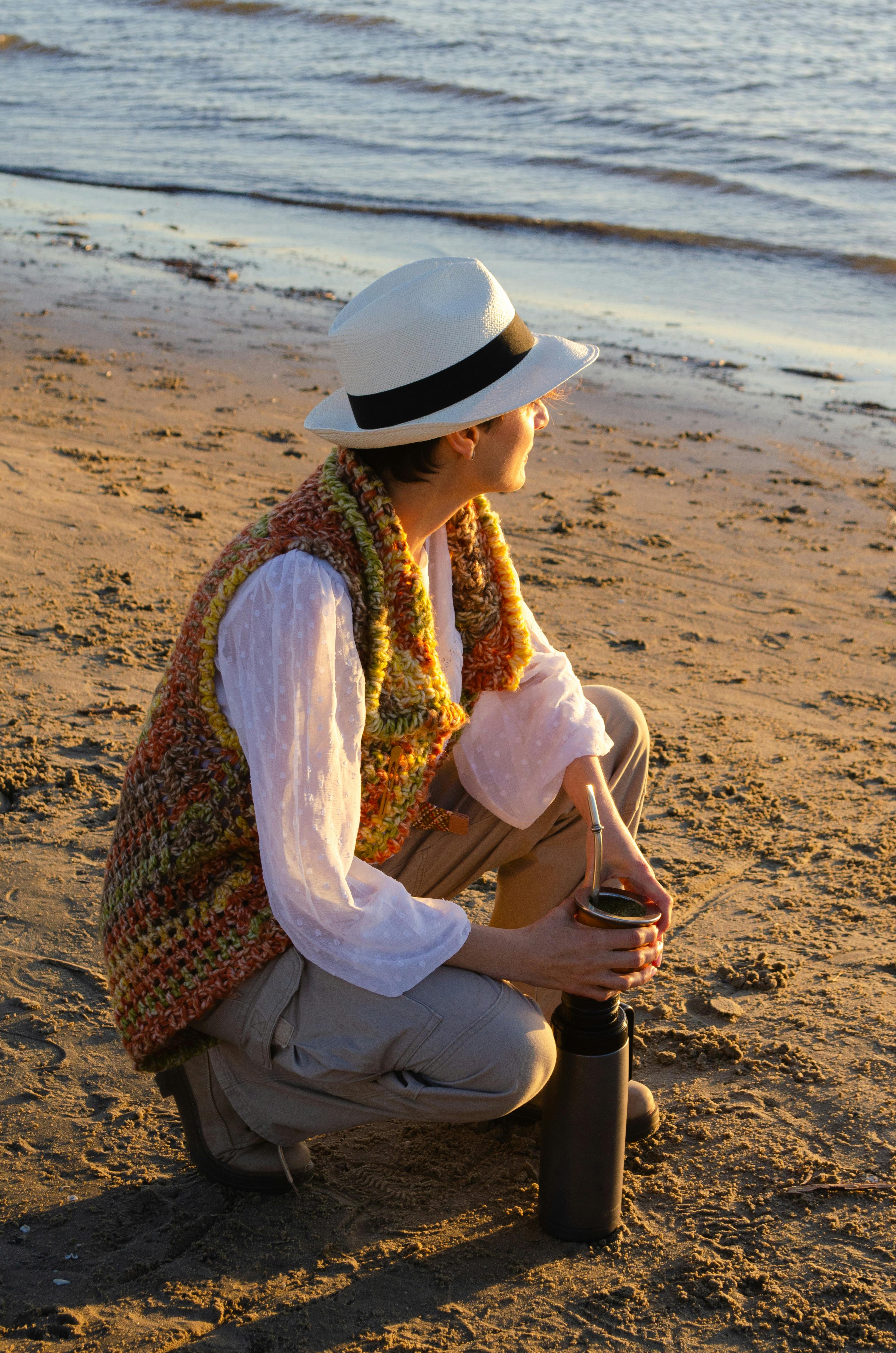 Gratuit Une personne est assise sur la plage de Montevideo au coucher du soleil, savourant une boisson traditionnelle, le maté. Photos