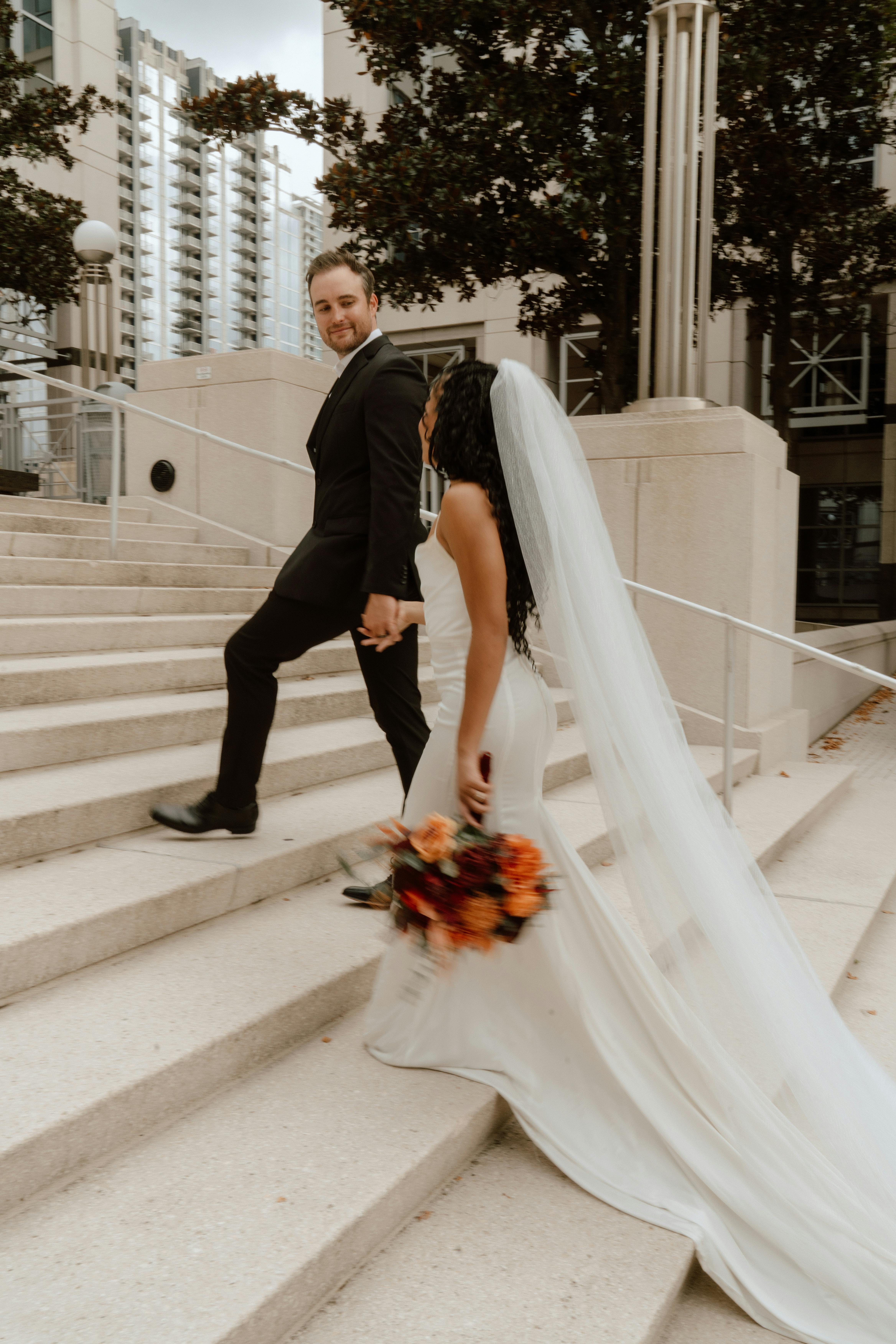 무료 우아한 옷차림을 한 신혼 부부가 도시의 계단에서 포즈를 취하며 올랜도의 현대적이고 낭만적인 순간을 포착했습니다. 스톡 사진