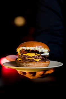 Close-up of a savory double cheeseburger with bacon, held on a plate, perfect for food lovers.