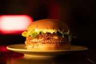 Close-up of a gourmet cheeseburger with lettuce and sauce on a plate, highlighted by soft lighting.