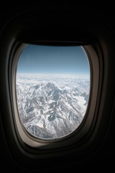 A breathtaking view of snow-covered mountains through an airplane window.