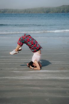 Woman performing a headstand yoga pose on a tranquil sandy beach.