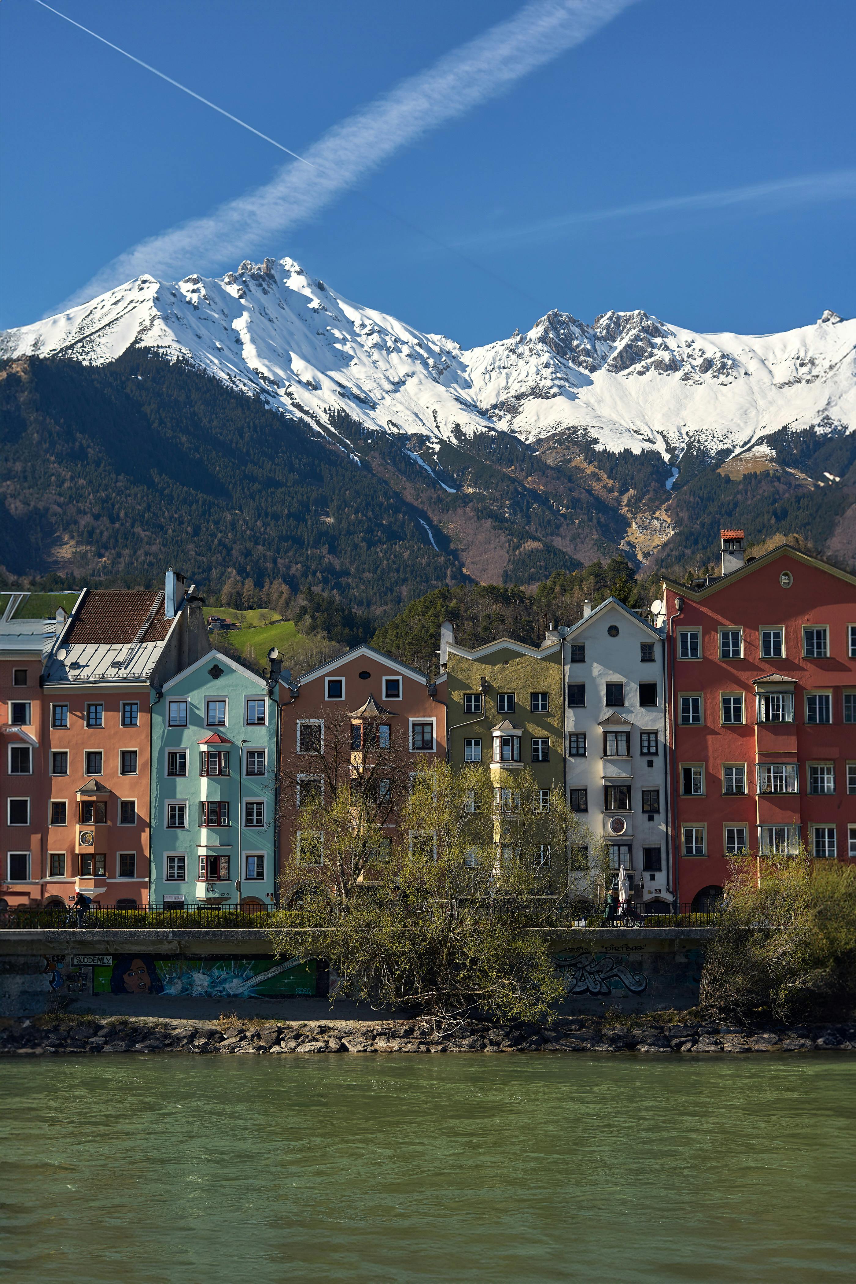 Scenic view of colorful buildings along a river with snow-capped mountains in the background.