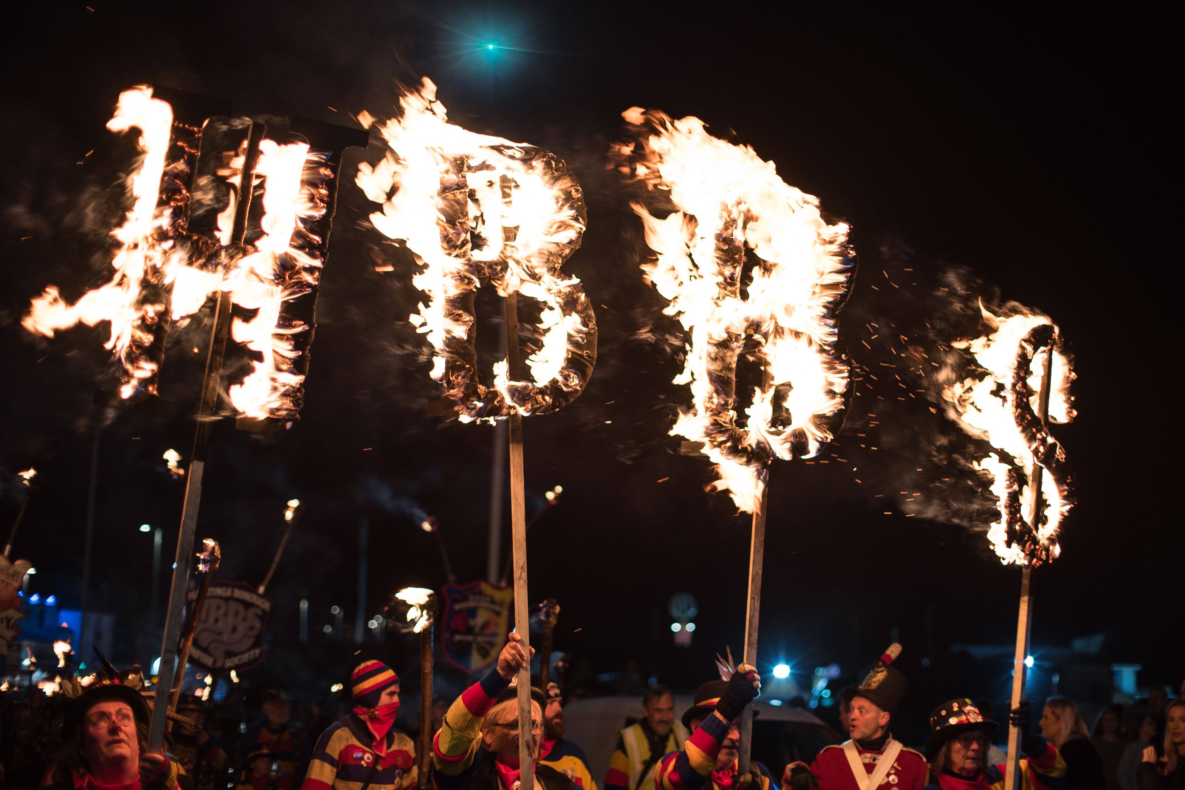 Dramatic torchlight parade at night featuring burning letters and colorful attire in a festive atmosphere.