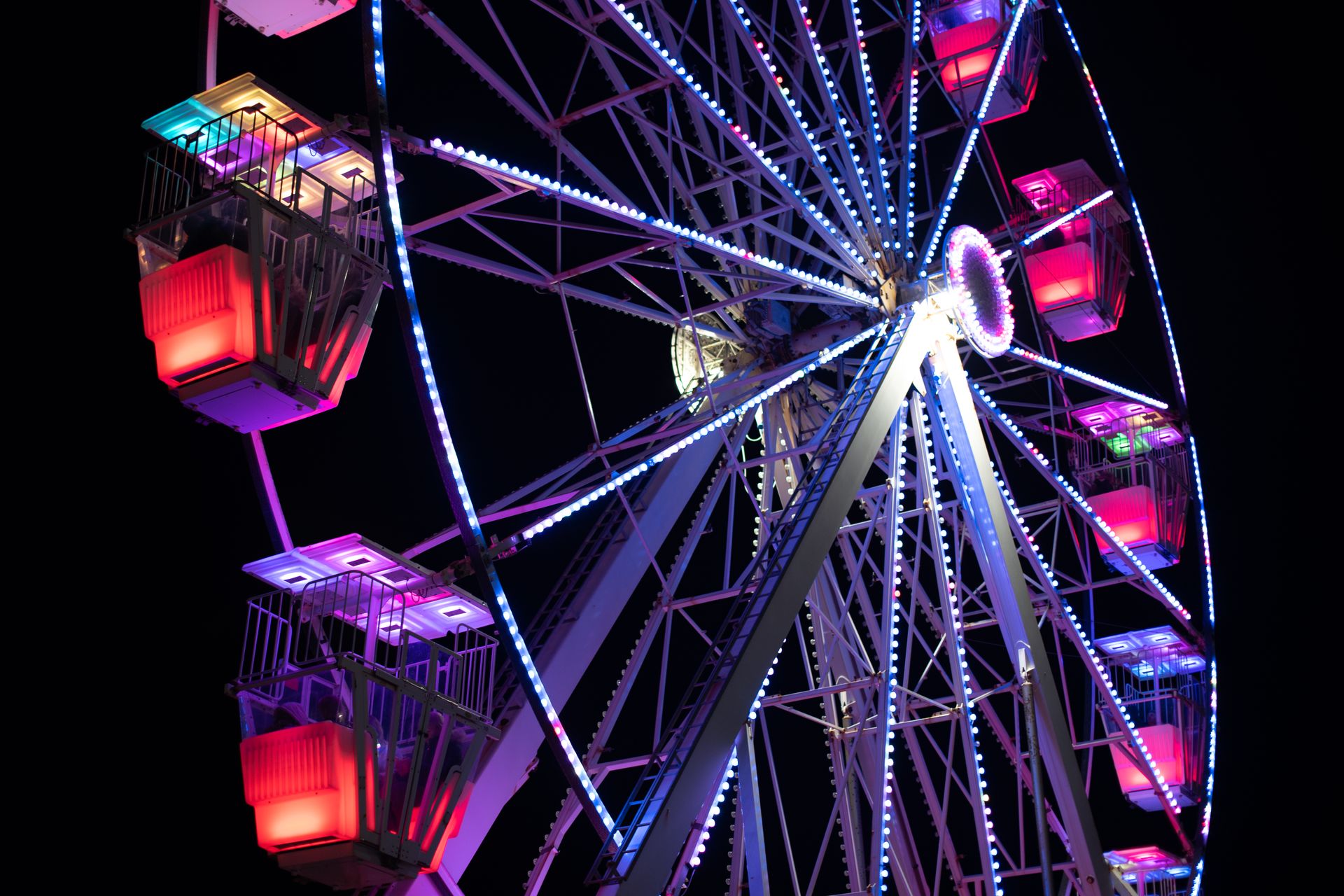 A brightly lit Ferris wheel glows against the night sky, with vivid neon colors reflecting off its metallic frame.