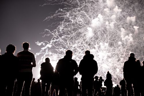 Free Silhouetted people watch dazzling fireworks illuminating the night sky with vibrant colors. Stock Photo