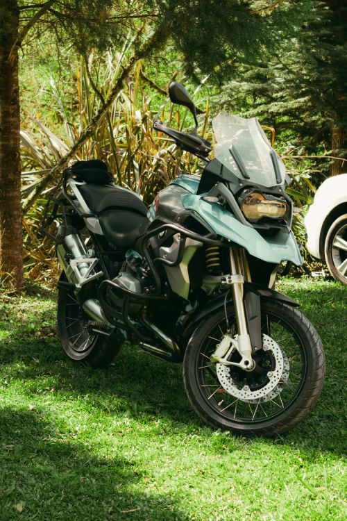 Free A rugged adventure motorcycle parked on lush green grass in a forest setting, ideal for travel enthusiasts. Stock Photo