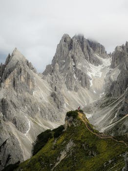 A lone hiker on a lush path in the dramatic Alpine mountains, shrouded in mist.