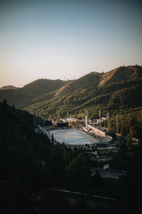 Free A vast mountain valley with a stadium, captured at sunset with shadows casting over lush green hills. Stock Photo