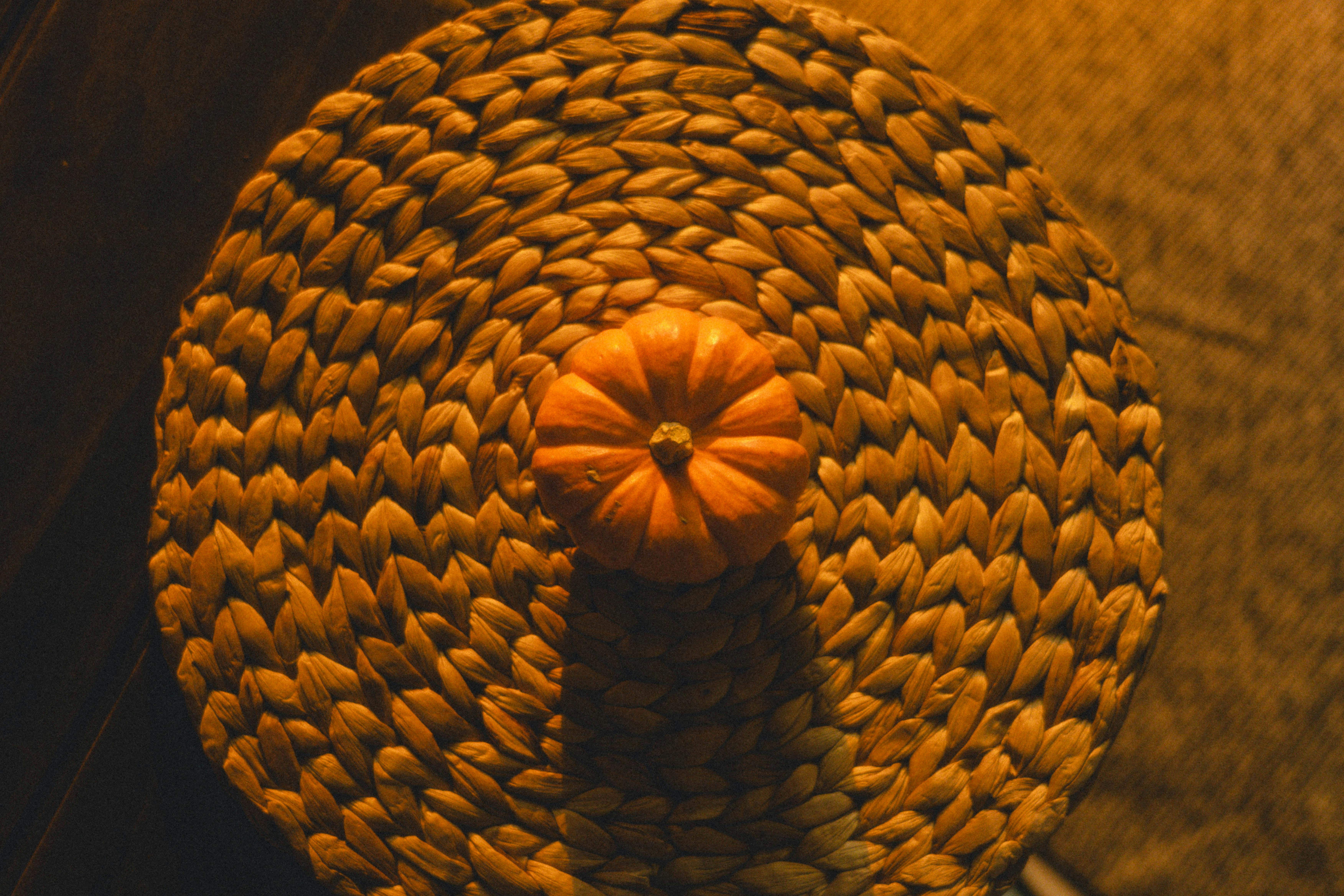 gratis Herfstmini-pompoen op een geweven mat met warme verlichting, perfect voor herfstthema's. Stockfoto