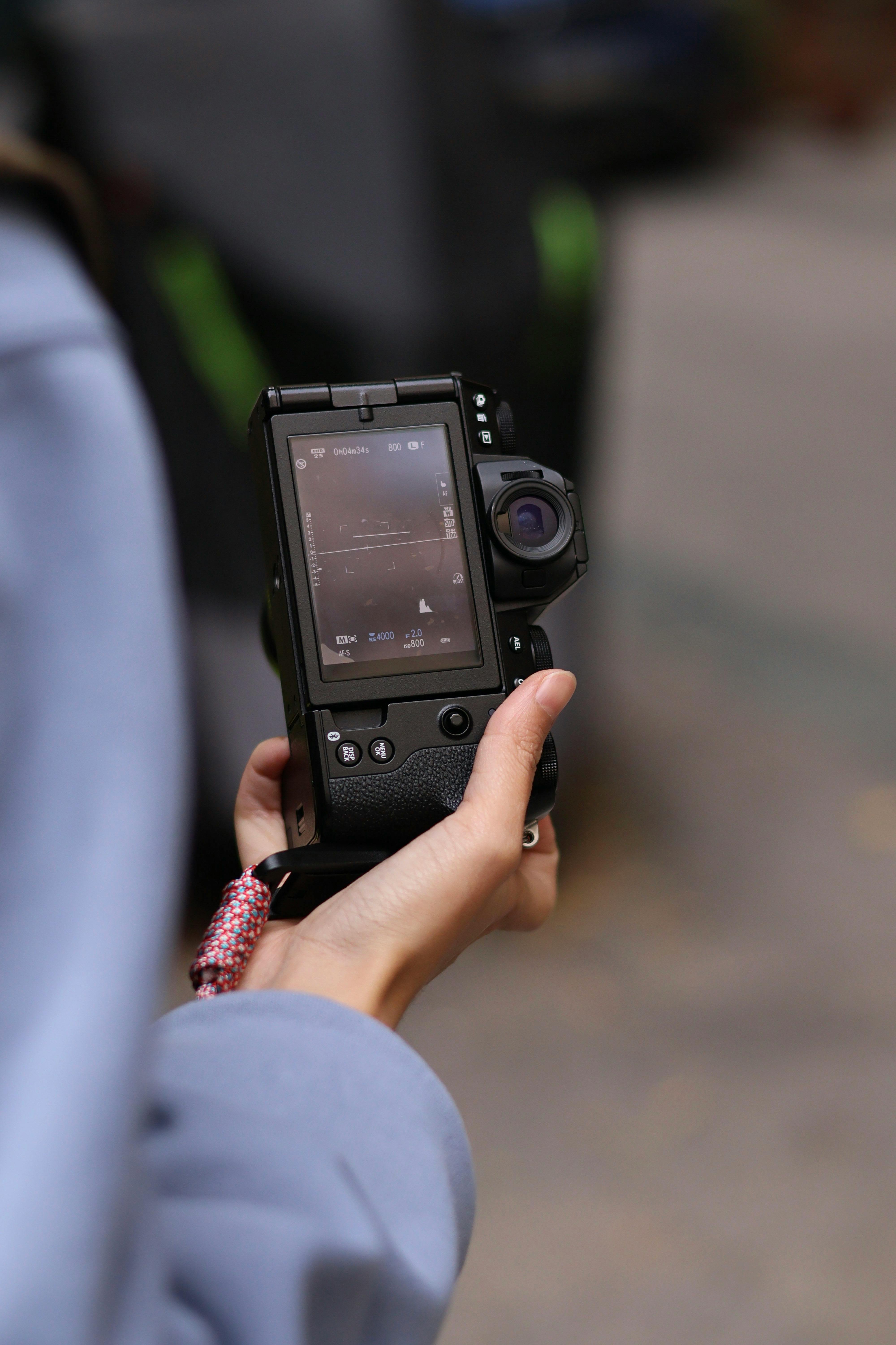 Free Person holding a camera outdoors, checking settings on a screen during the day. Stock Photo