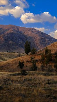 A serene mountain view with rugged terrain and sparse trees under a vivid blue sky.