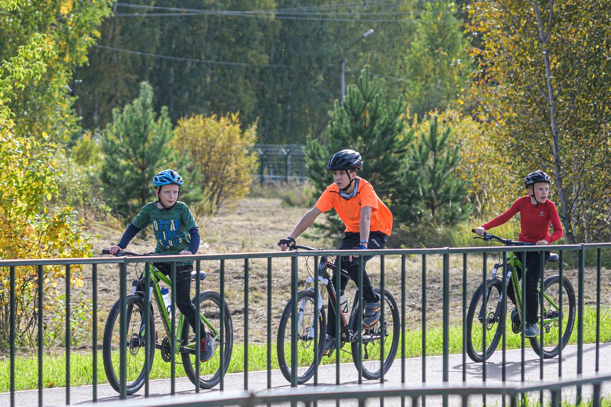 Three kids riding bikes together on a paved path wearing properly fitted helmets on the way to school