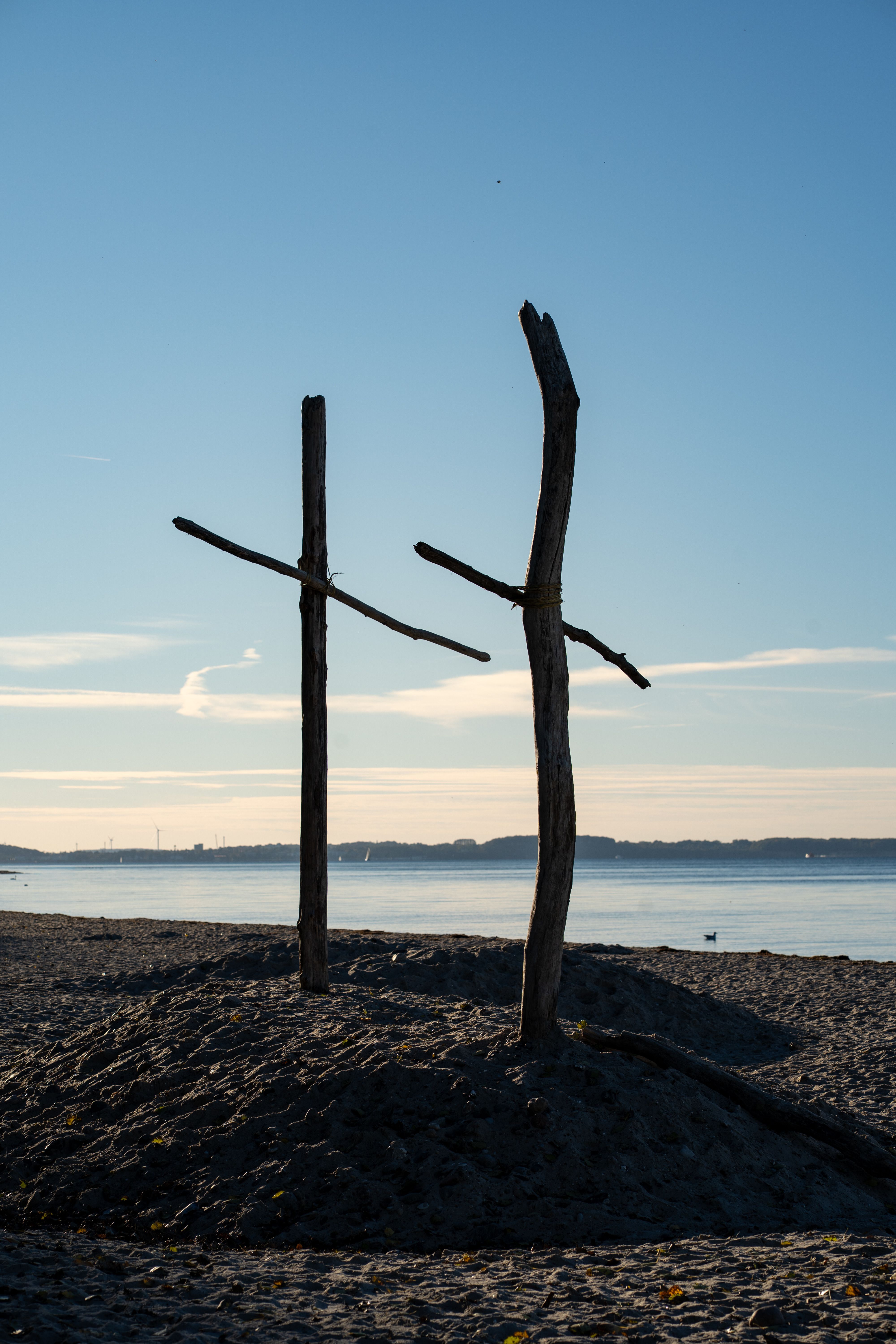 Two rustic wooden crosses on a sandy beach with a tranquil sea backdrop.