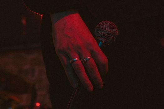 A close-up of a hand holding a microphone, enveloped in moody lighting, suggesting a performance atmosphere.