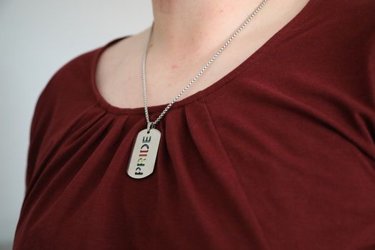 A close-up view of a silver Pride necklace worn over a maroon shirt, symbolizing LGBTQ pride.