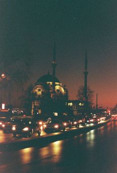 A vintage film photo of a mosque at twilight in İstanbul, Türkiye with traffic lights reflecting on wet pavement.