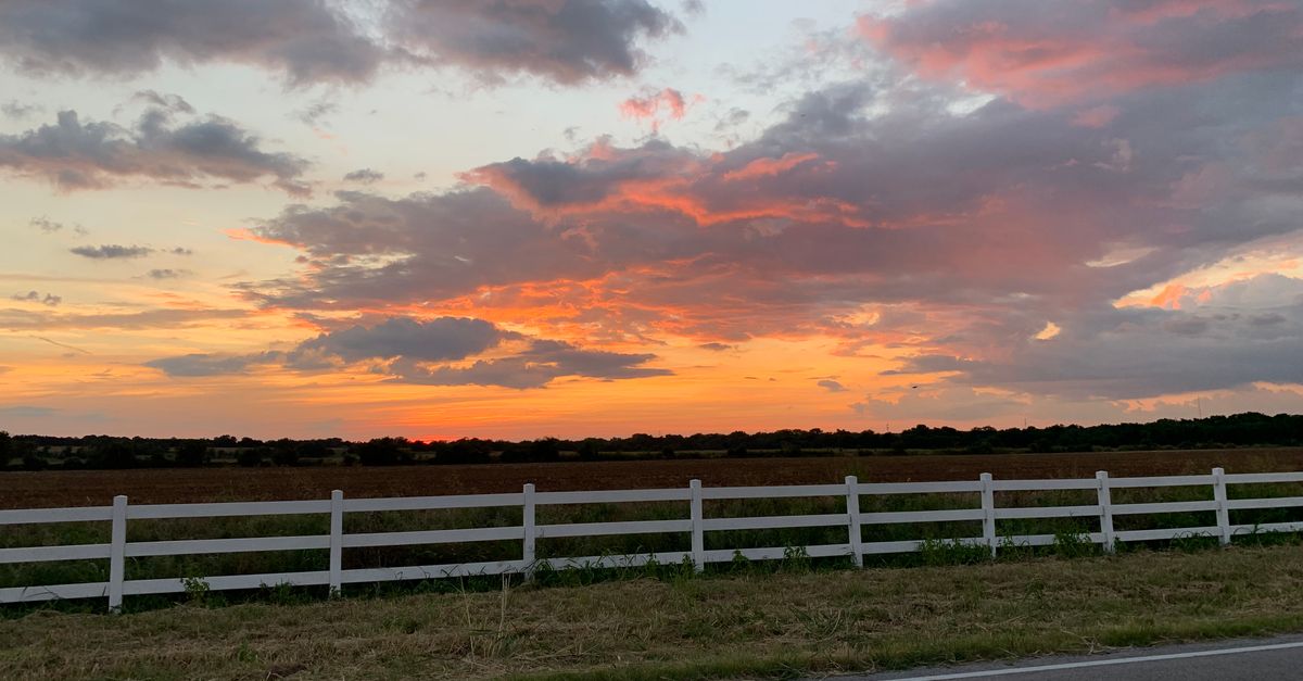 Breathtaking sunset over a Texas pasture with vivid colors and a white fence lining the road.