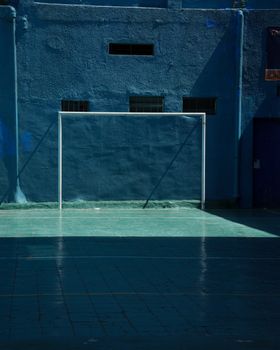 Blue sports court with goalpost and shadow play, capturing urban minimalism.