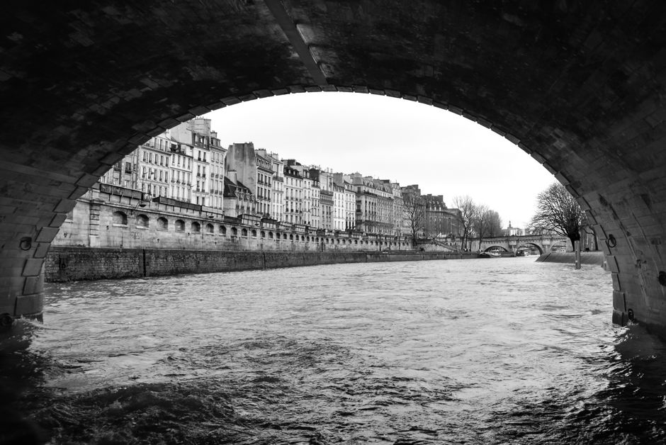 Scenic black and white view of River Seine and historic Parisian buildings from under a bridge.