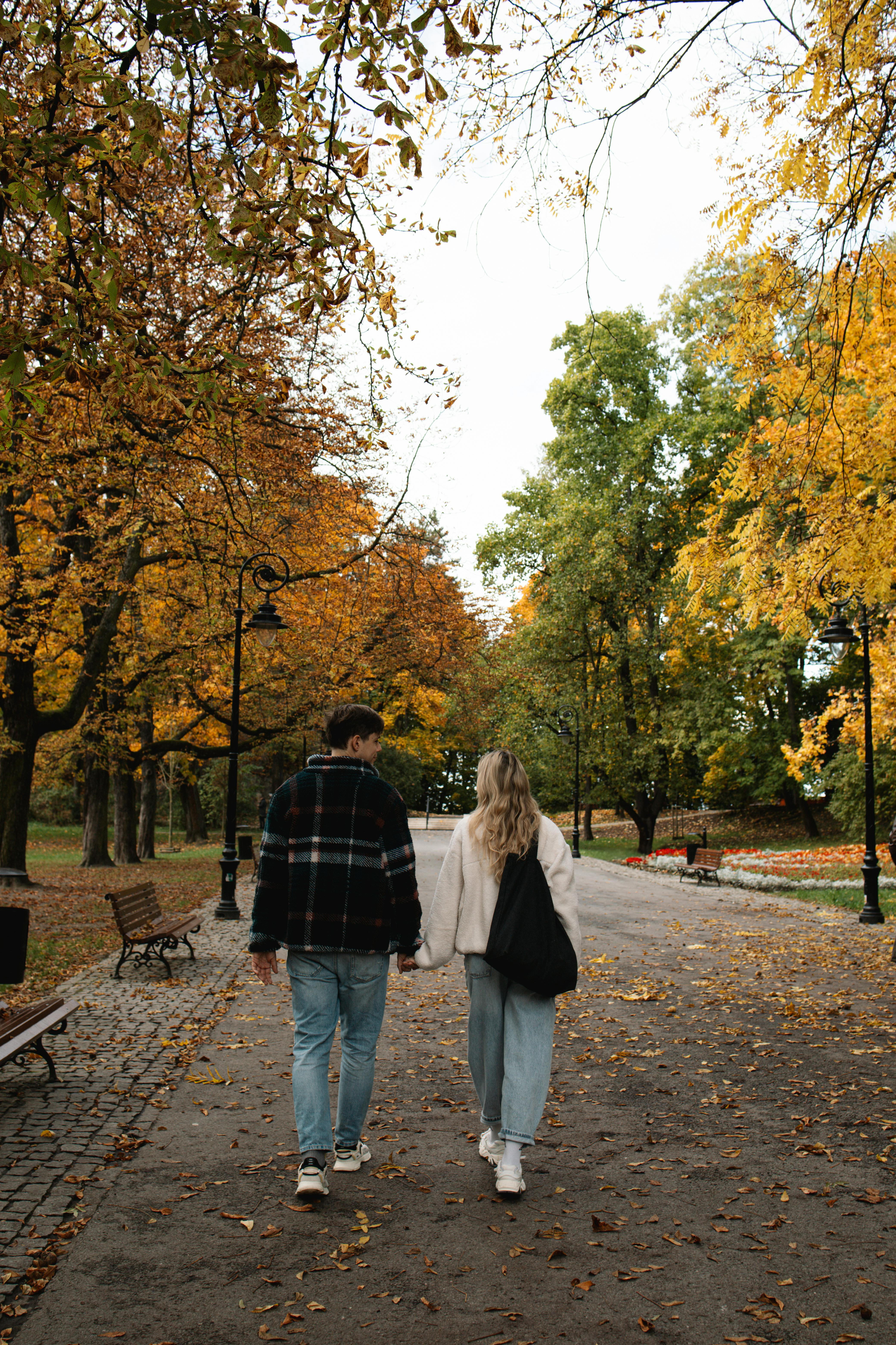 A romantic couple strolls hand in hand on a scenic autumn pathway surrounded by vibrant fall foliage.