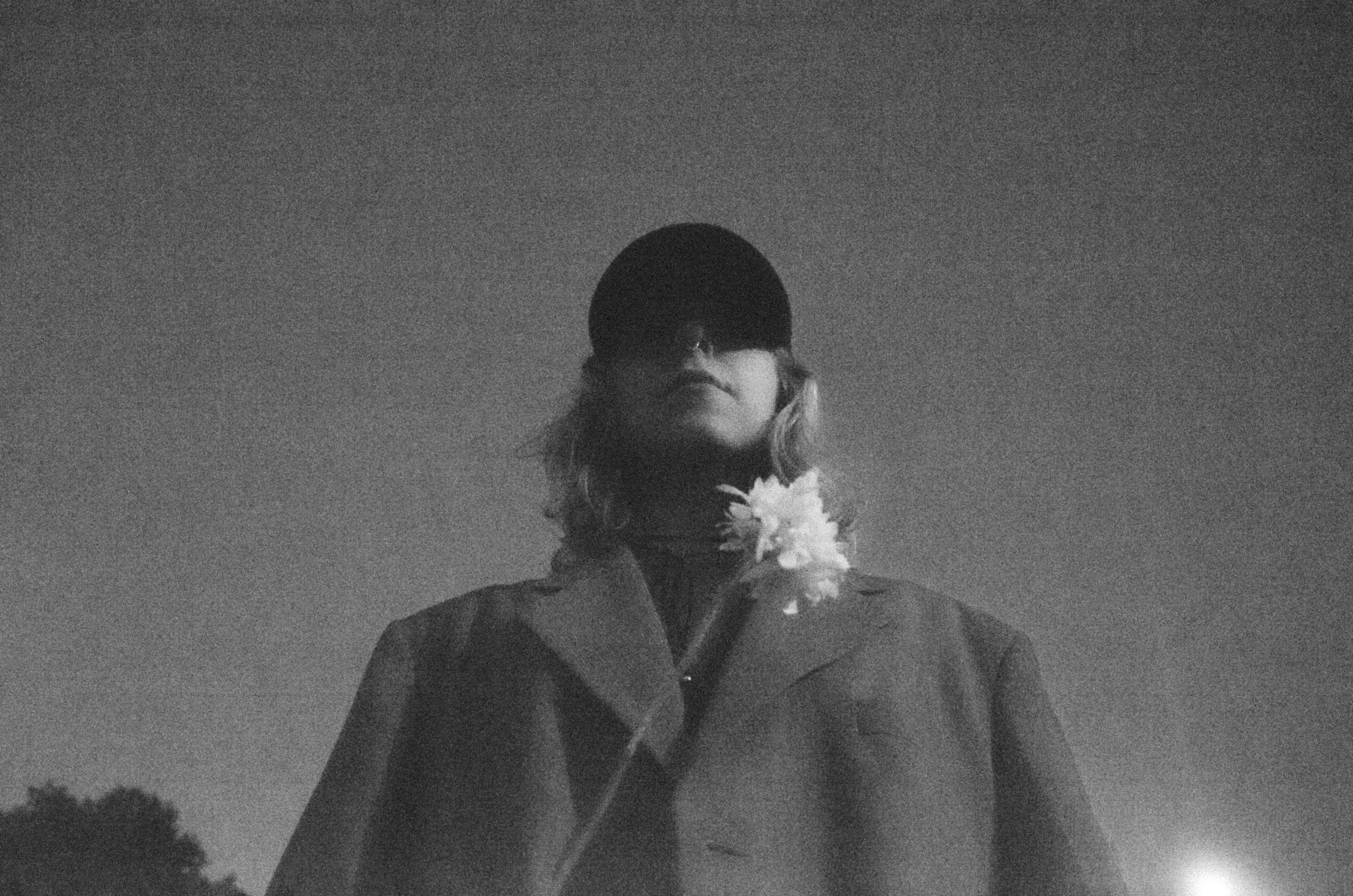 A mysterious figure in black and white attire with a flower in an urban setting.