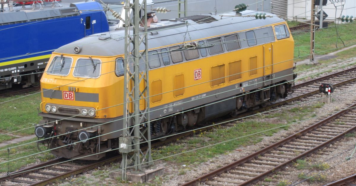 Old yellow diesel locomotive on tracks by DB in a train yard.
