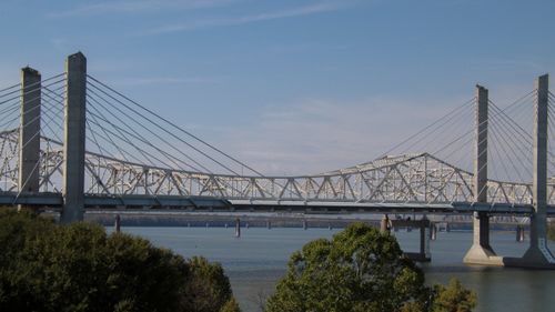 Free Scenic view of a cable-stayed bridge spanning across a tranquil river under a clear blue sky. Stock Photo