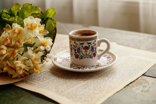 Free Artistic floral tea cup with coffee beside a daffodil bouquet on vintage paper. Stock Photo