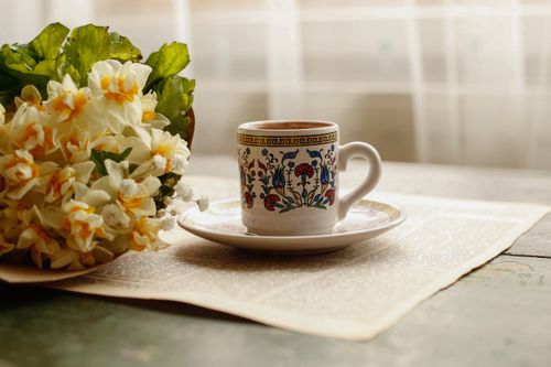 Free A decorative tea cup with floral patterns next to daffodils on a table. Stock Photo