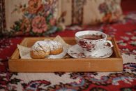 Delicate floral teacup with pastry on ornate carpet tray, evoking classic tea time.