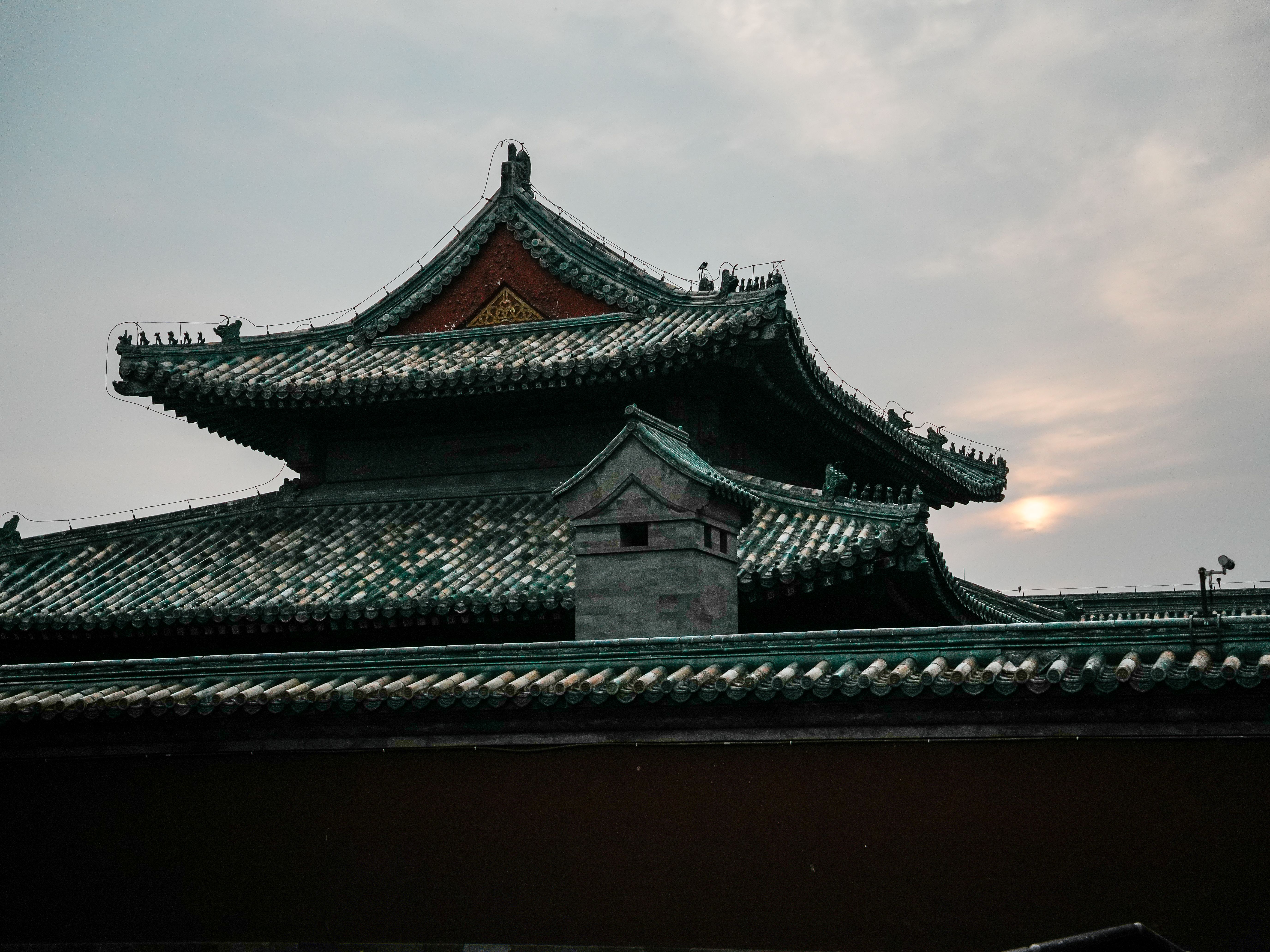A traditional Chinese temple roof silhouetted against a serene sunset sky.