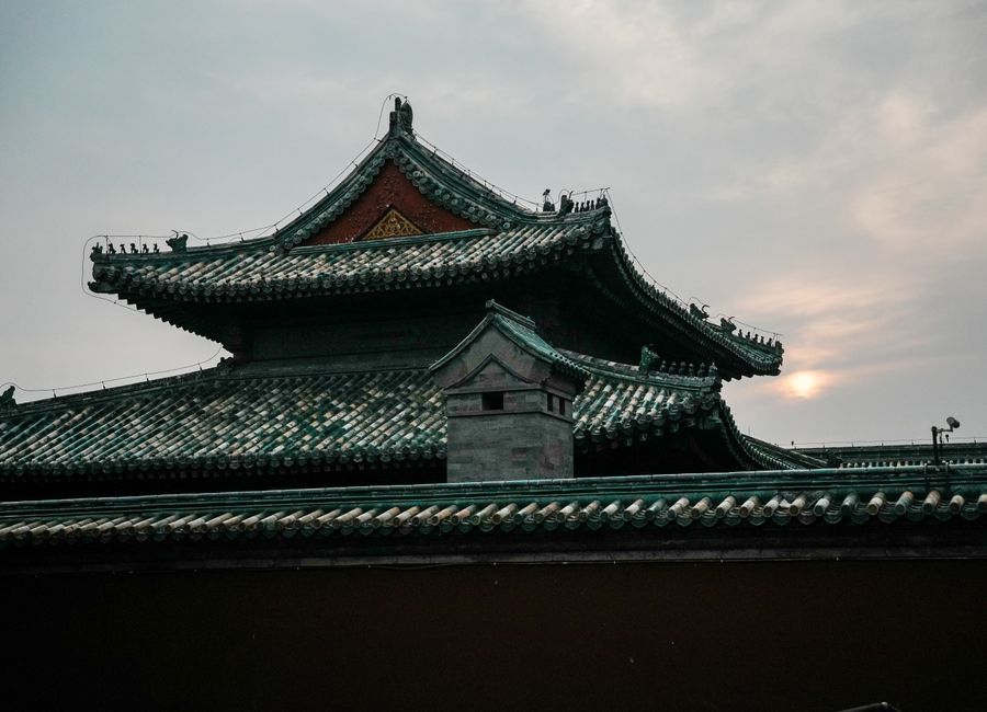A traditional Chinese temple roof silhouetted against a serene sunset sky.