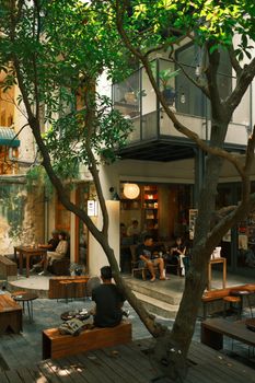 Peaceful outdoor cafe courtyard in New Zealand with people relaxing and socializing under trees.