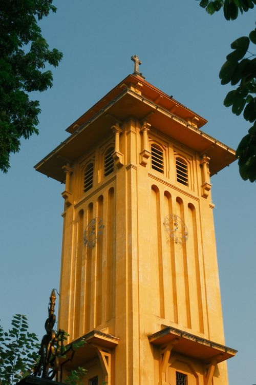 Free Tall yellow church tower with intricate design set against a blue sky. Stock Photo