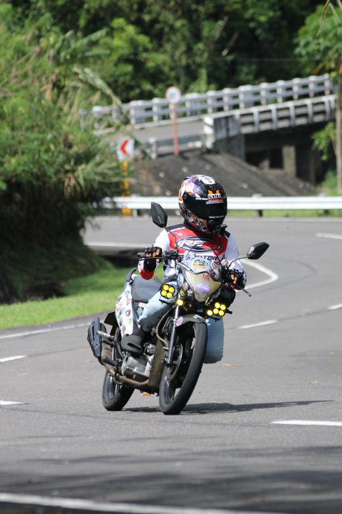 Free Motorcyclist navigating a winding road with greenery, daytime shot. Stock Photo