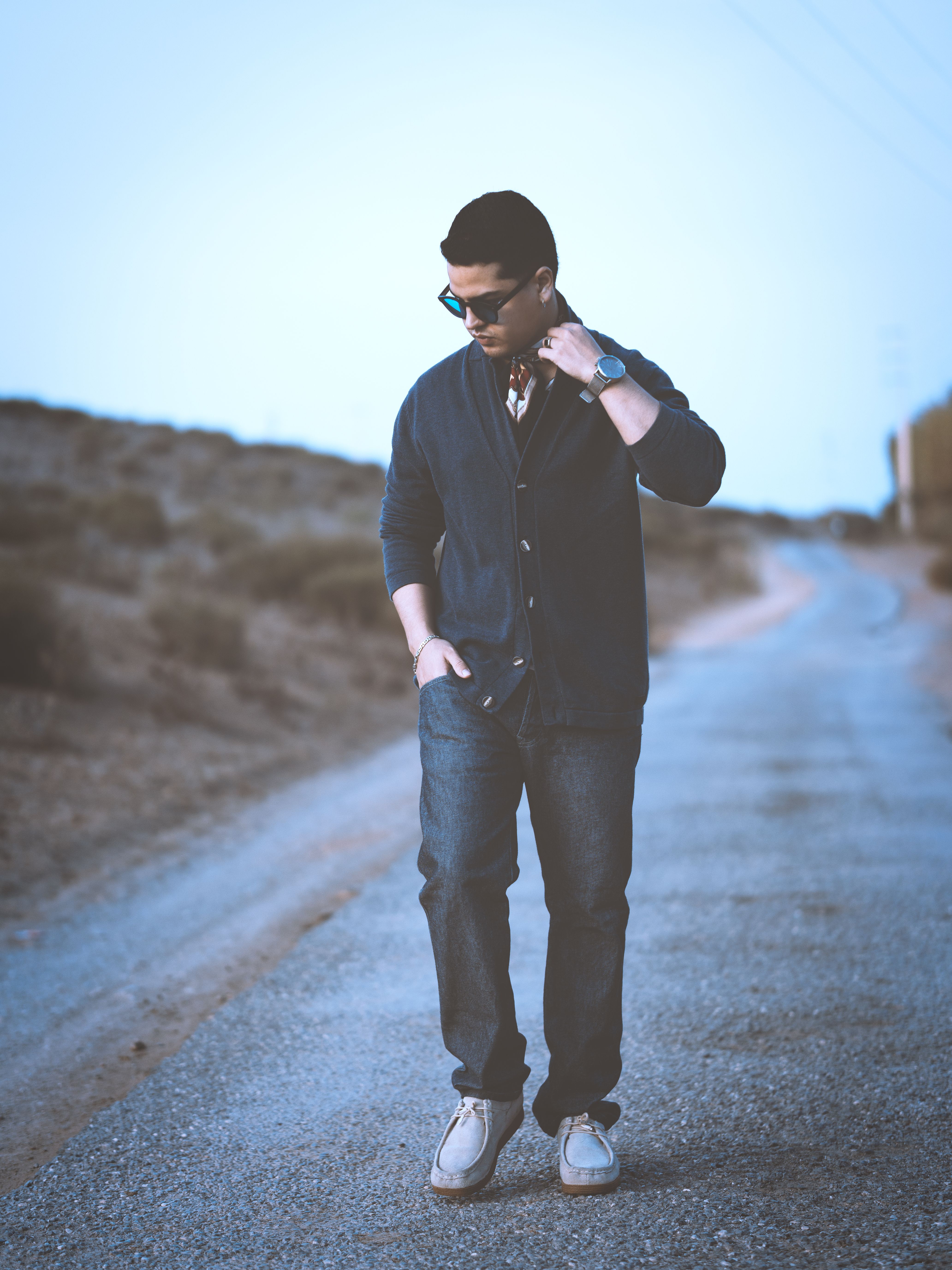 Casually dressed man in glasses walking a rural road at twilight, exuding a cool, modern vibe.