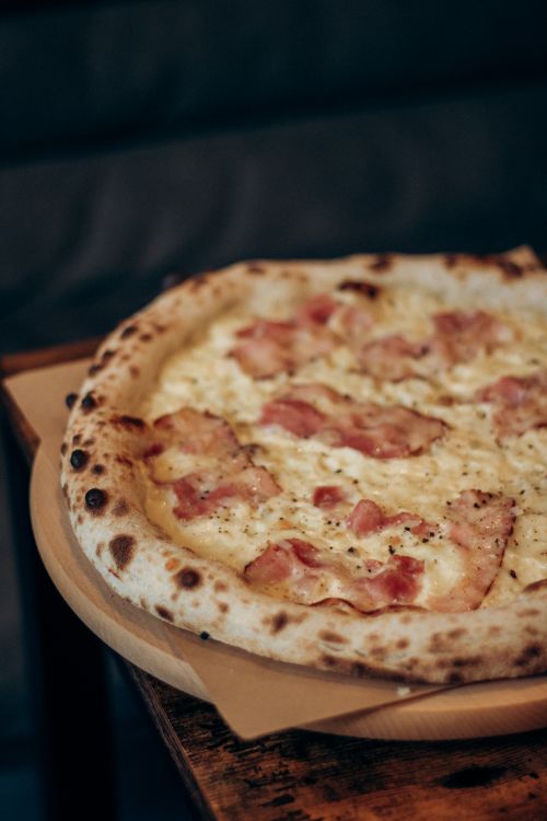 Free Delicious crispy bacon and cheese pizza on a wooden board, perfect for gourmet cuisine. Stock Photo